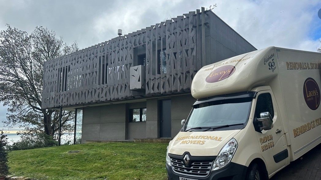A white moving van parked in front of a modern gray house with vertical wooden slats.