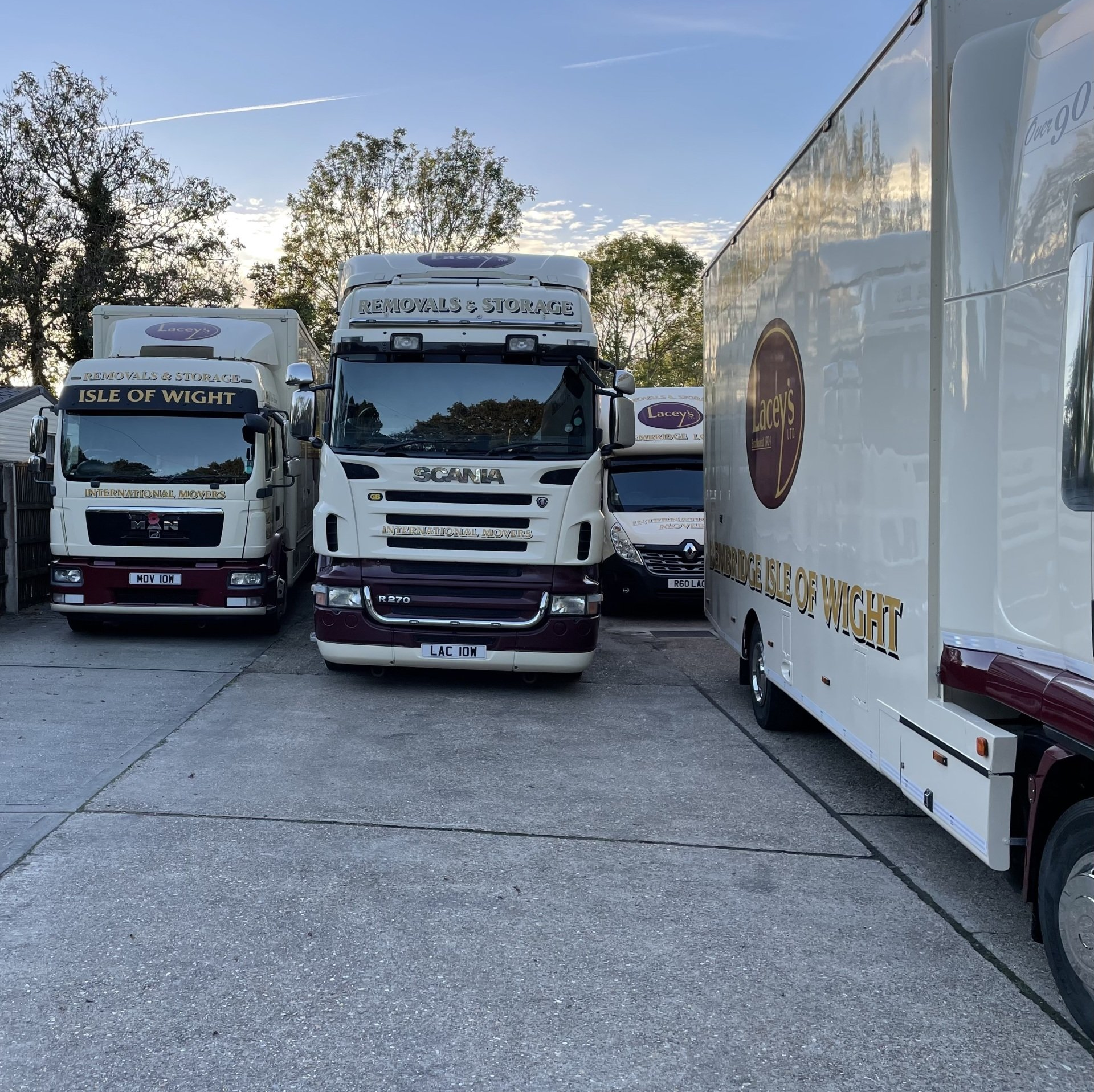 Trucks parked in a lot, various sizes and brands. Cream-colored with maroon accents. Daytime.