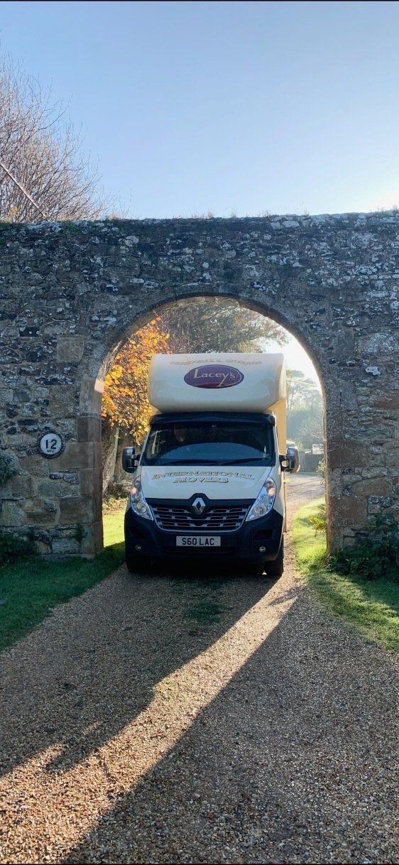 A white van with a logo on top driving through a stone archway.