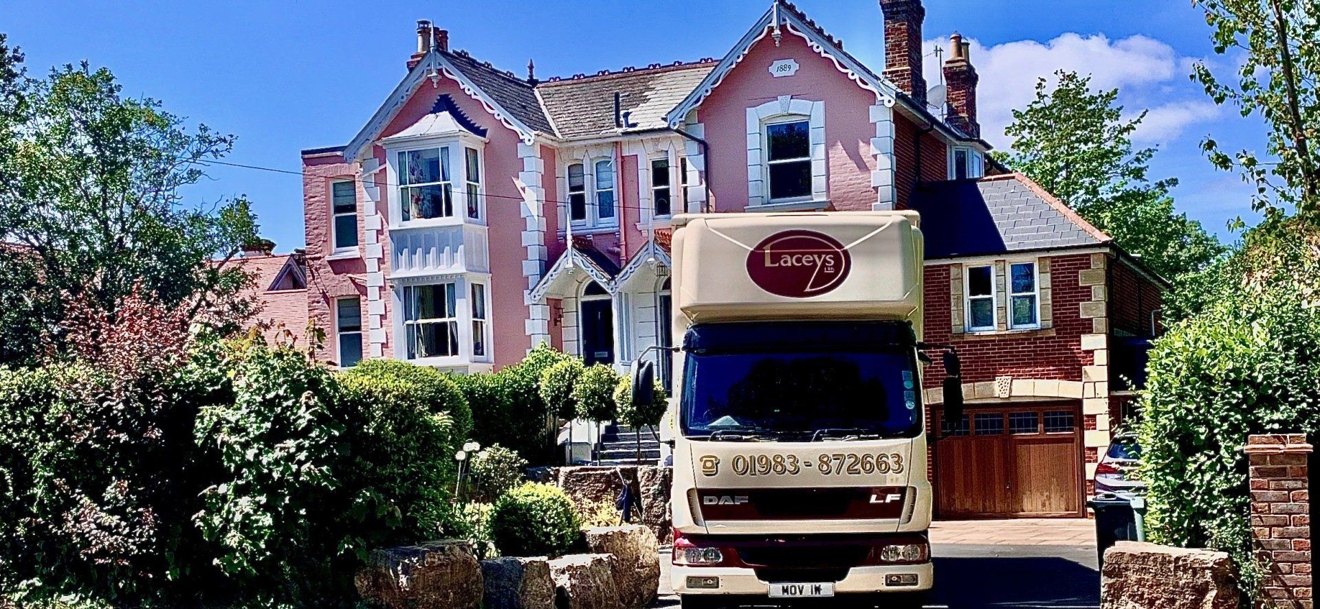 Moving truck in front of a pink house on a sunny day.