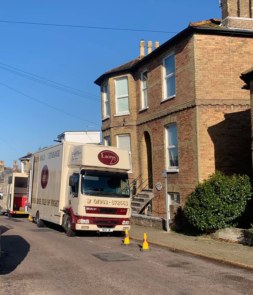 Delivery truck parked on a street next to a brick building; yellow cones in front.
