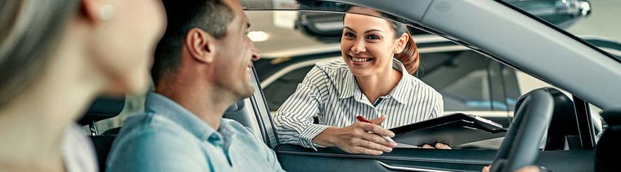 Cliente sonriendo mientras habla con un hombre en una sala de exposición de coches.