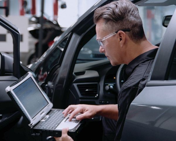 Técnico utilizando un ordenador portátil para diagnosticar un coche dentro de un taller de reparación de automóviles.