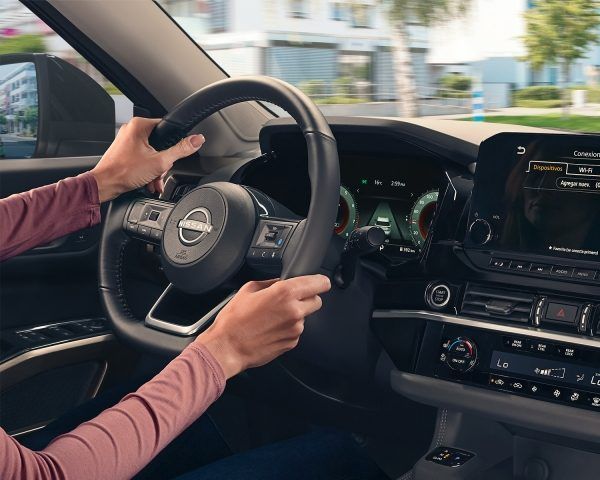 Manos del conductor sobre el volante de un Nissan dentro de un coche moderno, circulando por una calle de la ciudad.