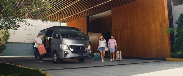 Personas descargan una furgoneta frente a un edificio moderno con paneles de madera.