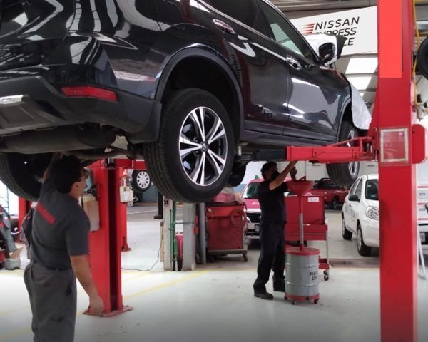 Un coche elevado en un elevador en un taller mecánico, con mecánicos trabajando debajo.