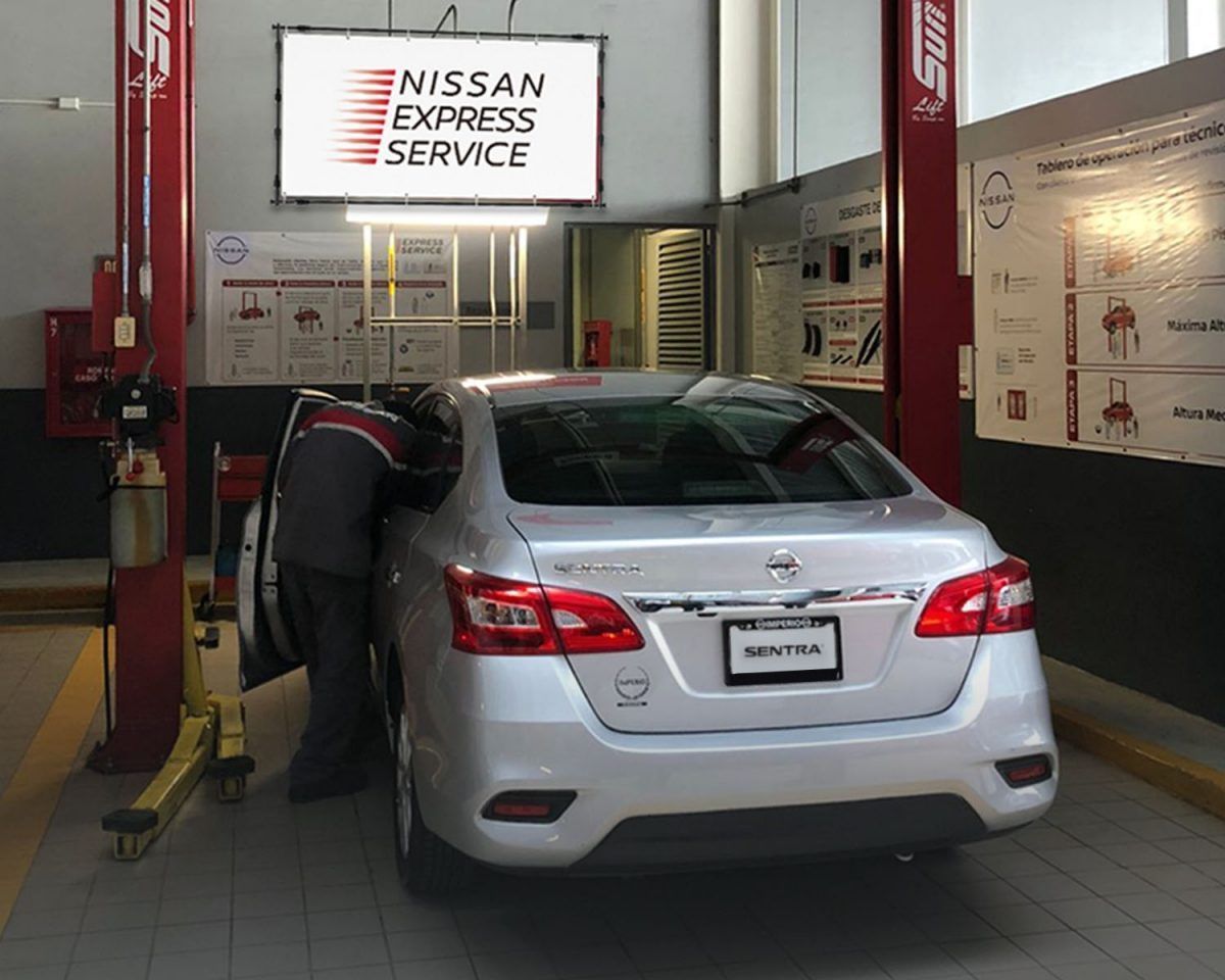 Sedán blanco en un taller de Nissan Express Service con una persona inclinada hacia el lado del conductor.