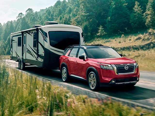 Un SUV rojo remolcando una gran caravana en una carretera forestal.
