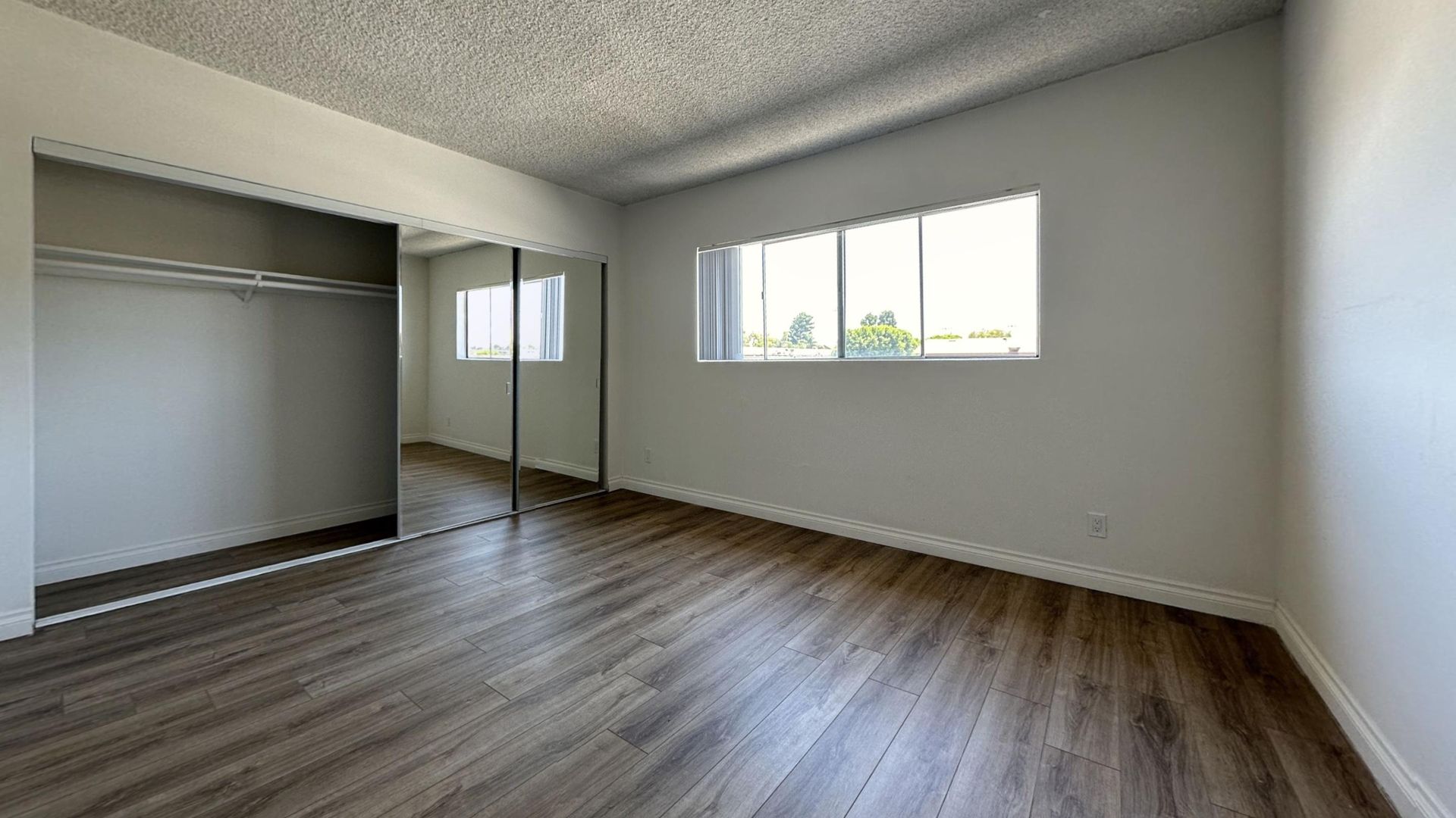 Empty bedroom with wood-look flooring, sliding closet doors, and a window.