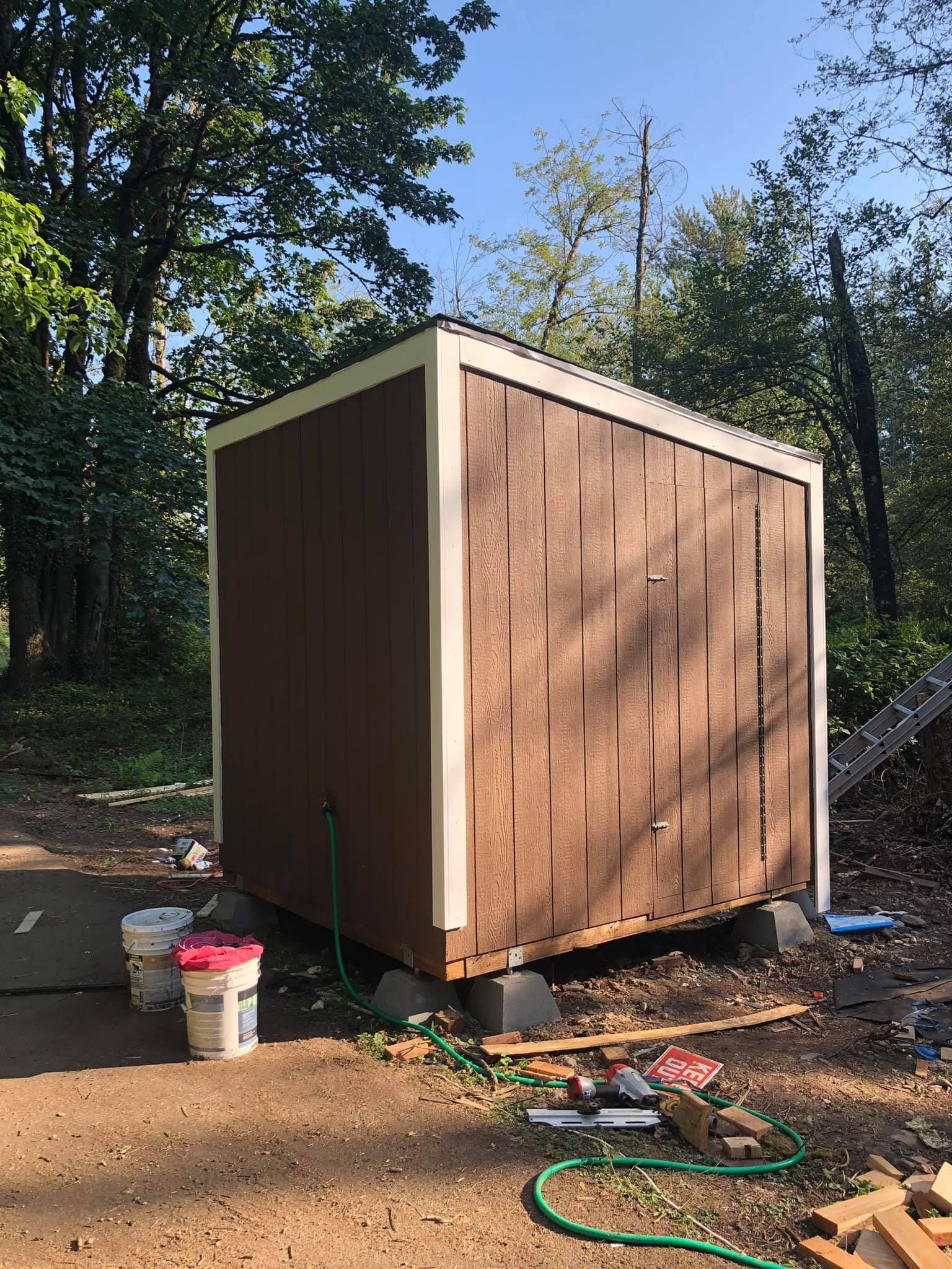 A small wooden shed is sitting in the middle of a dirt field.