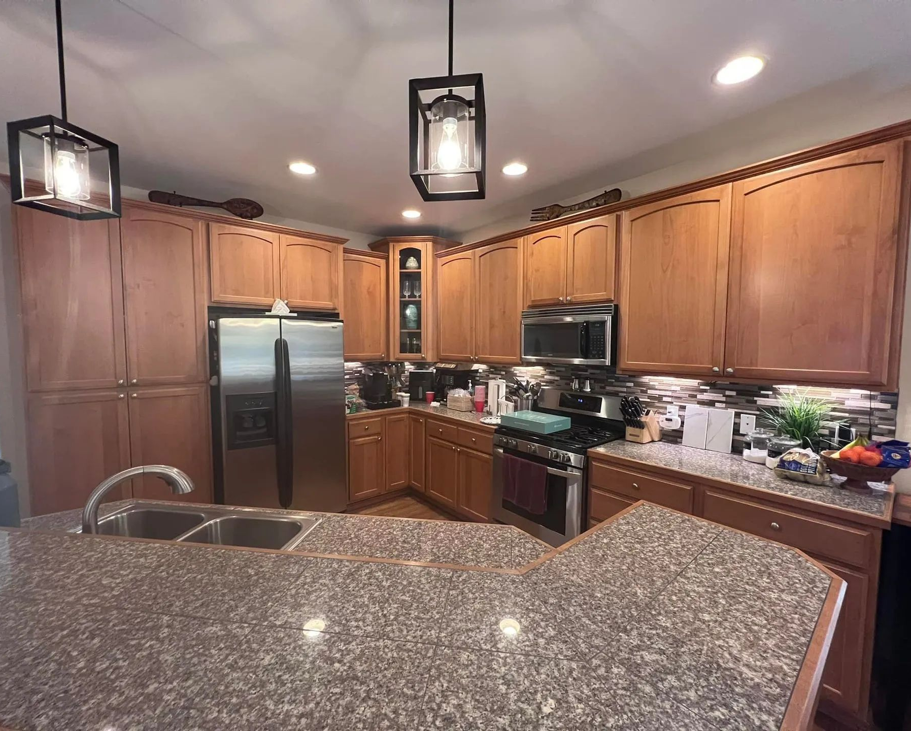 Spacious modern kitchen with wood cabinets, granite island, stainless appliances, and pendant lights.