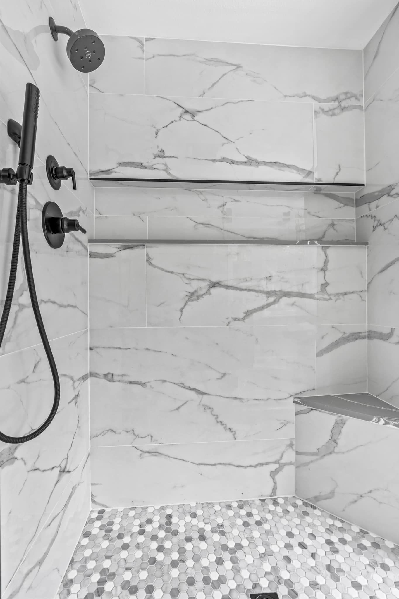A black and white photo of a shower with marble tiles and a shower head.