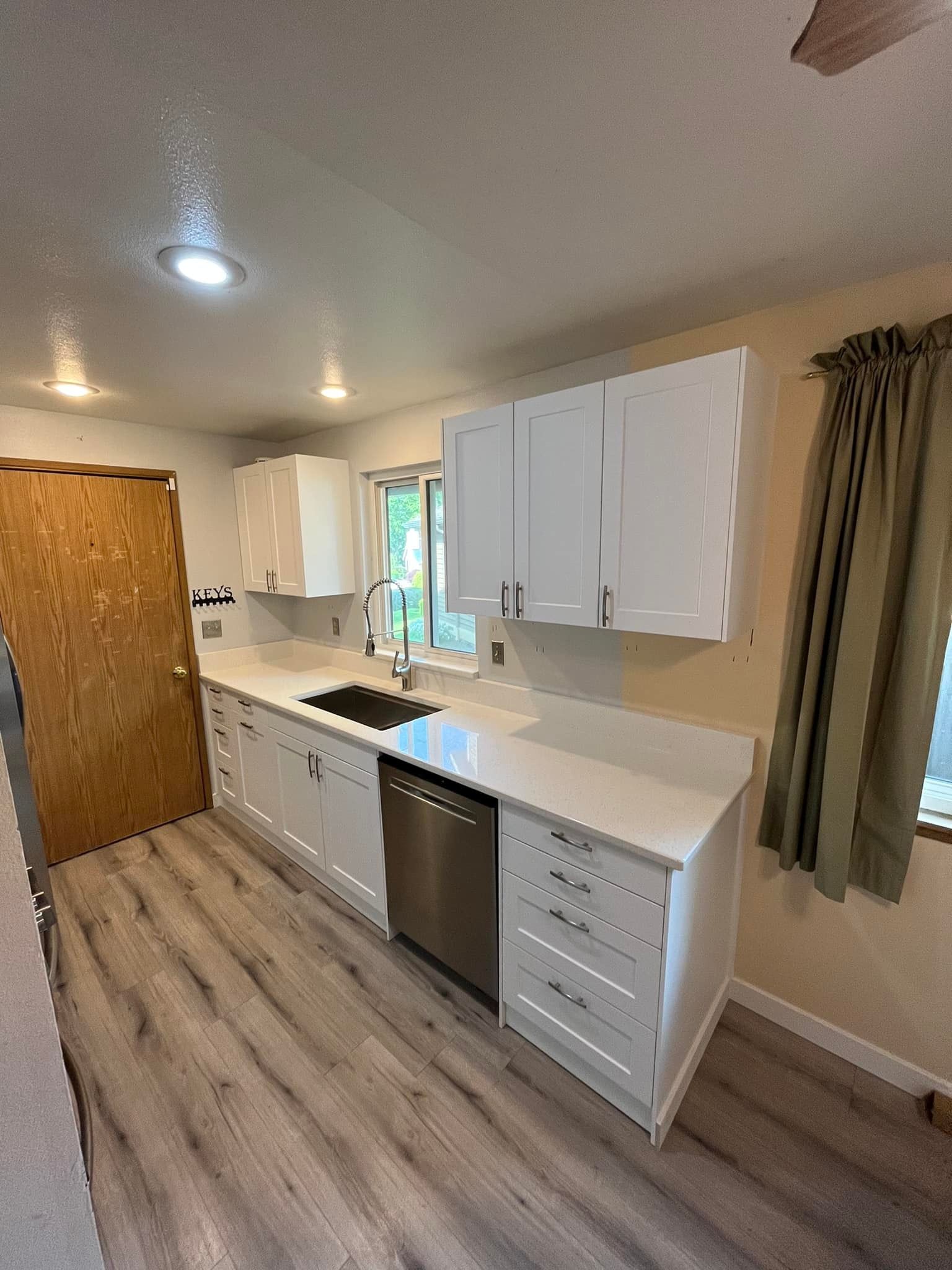 A kitchen with white cabinets , stainless steel appliances , a sink , and a window.