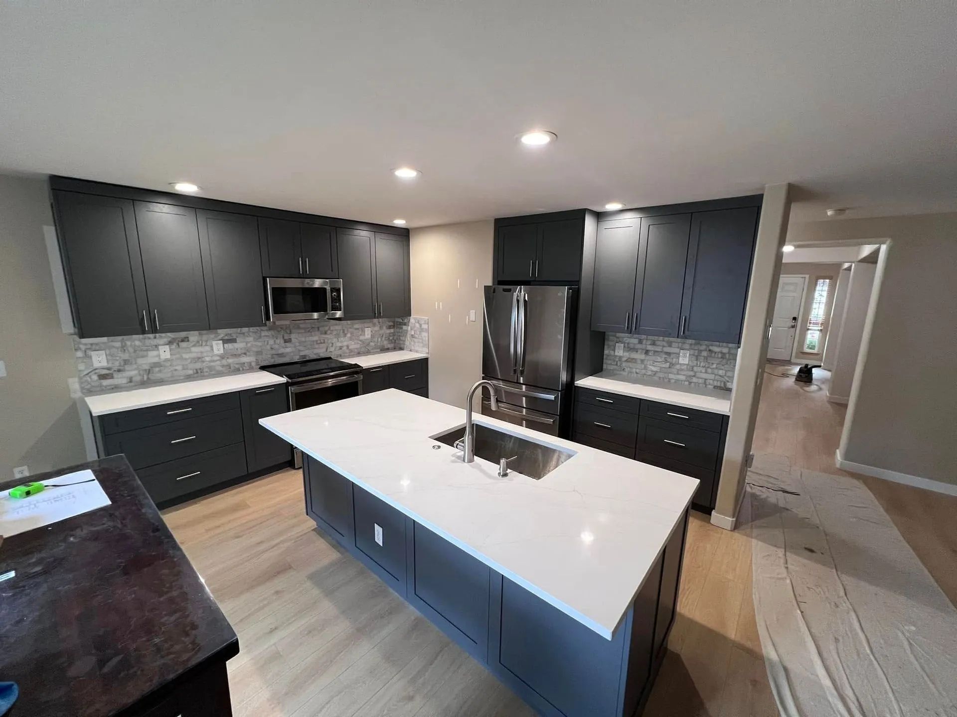Modern kitchen with dark cabinets, white island, stainless steel appliances, and light wood floors.