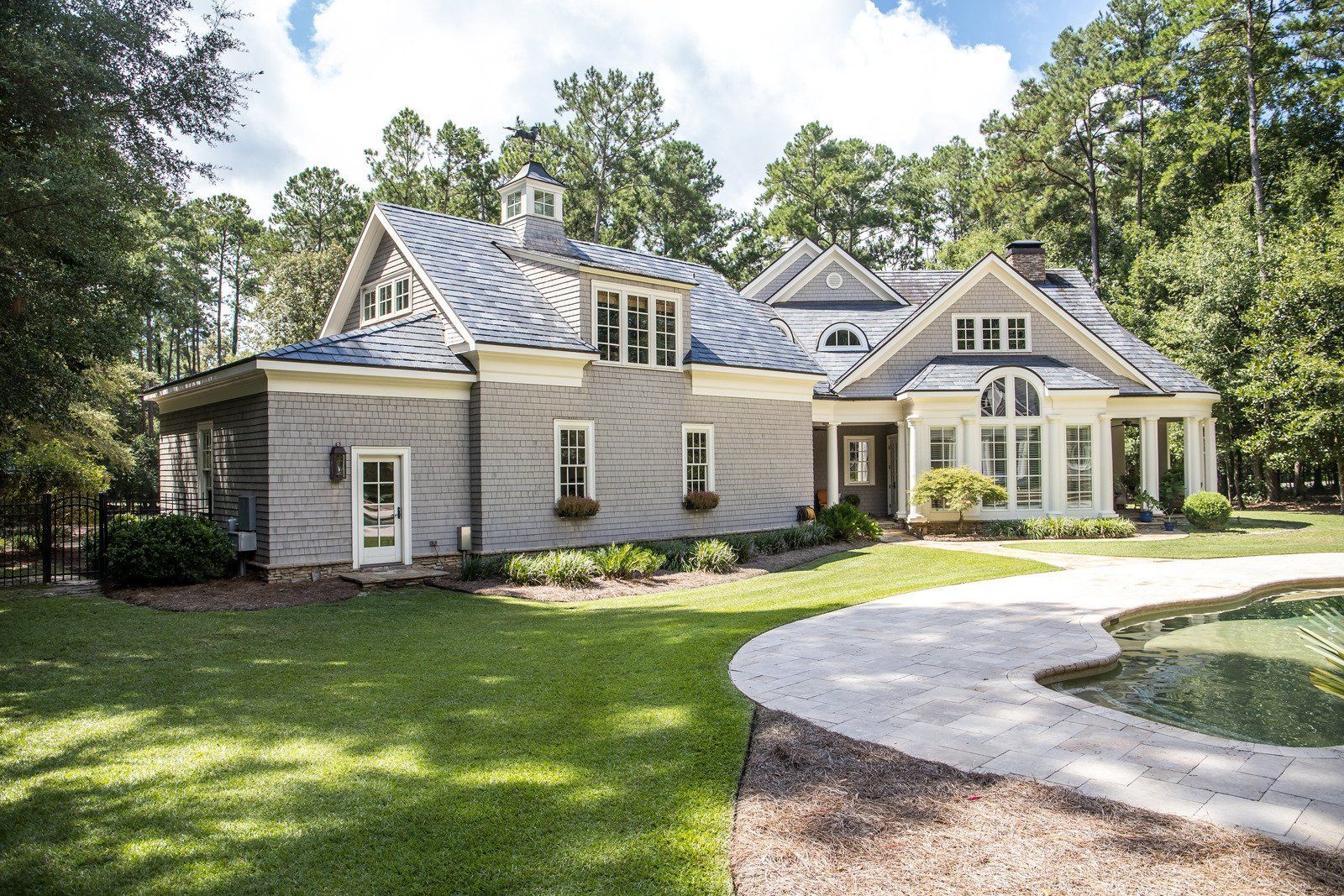 A large house with a walkway leading to it is surrounded by trees and grass.