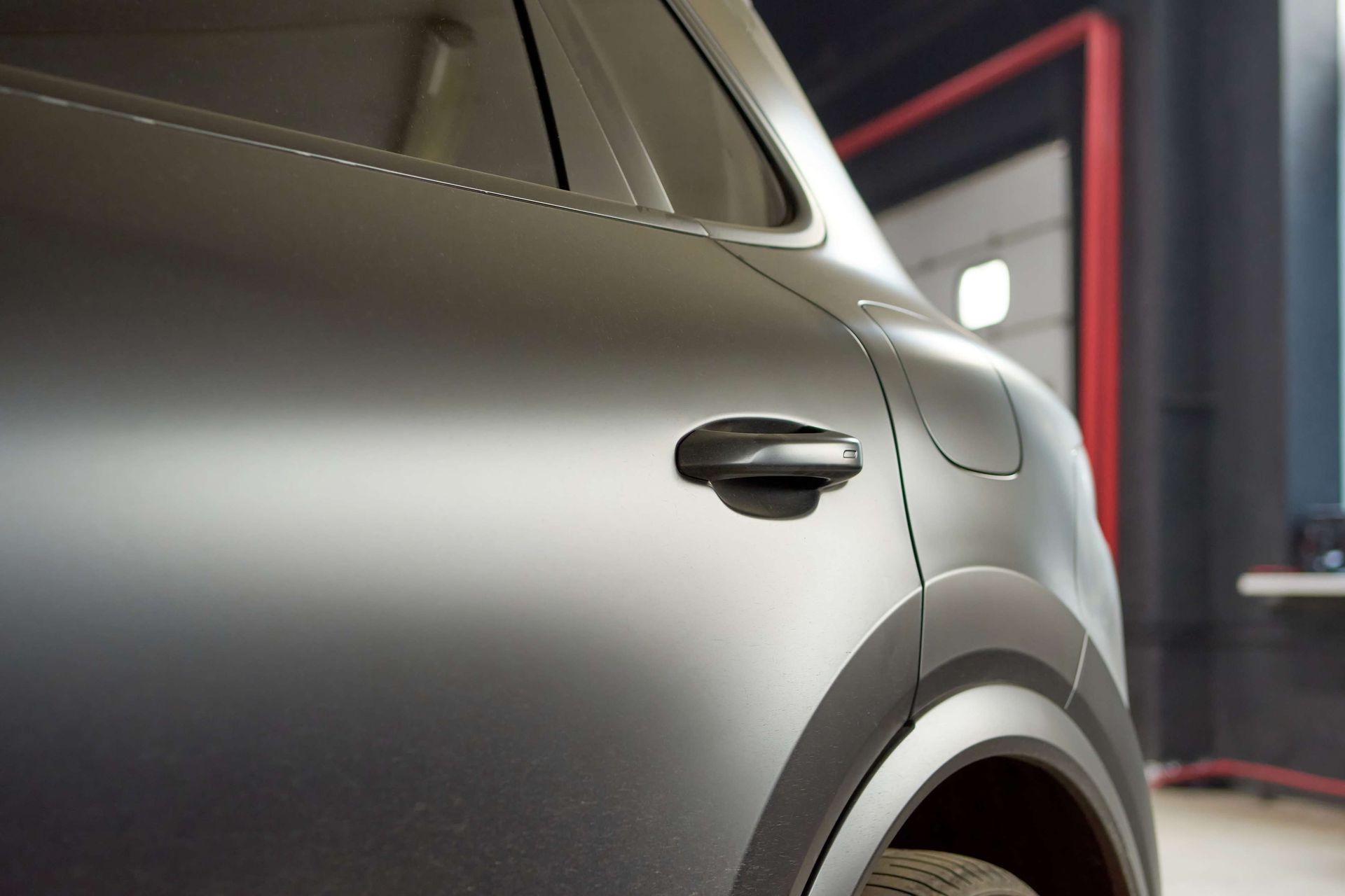 Matte gray car door, handle visible, in a garage setting.