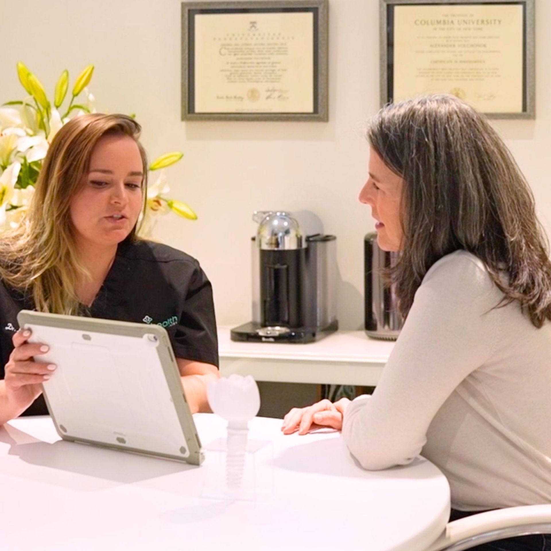 A healthcare provider discusses information on a tablet with a patient at a table in a clinic.