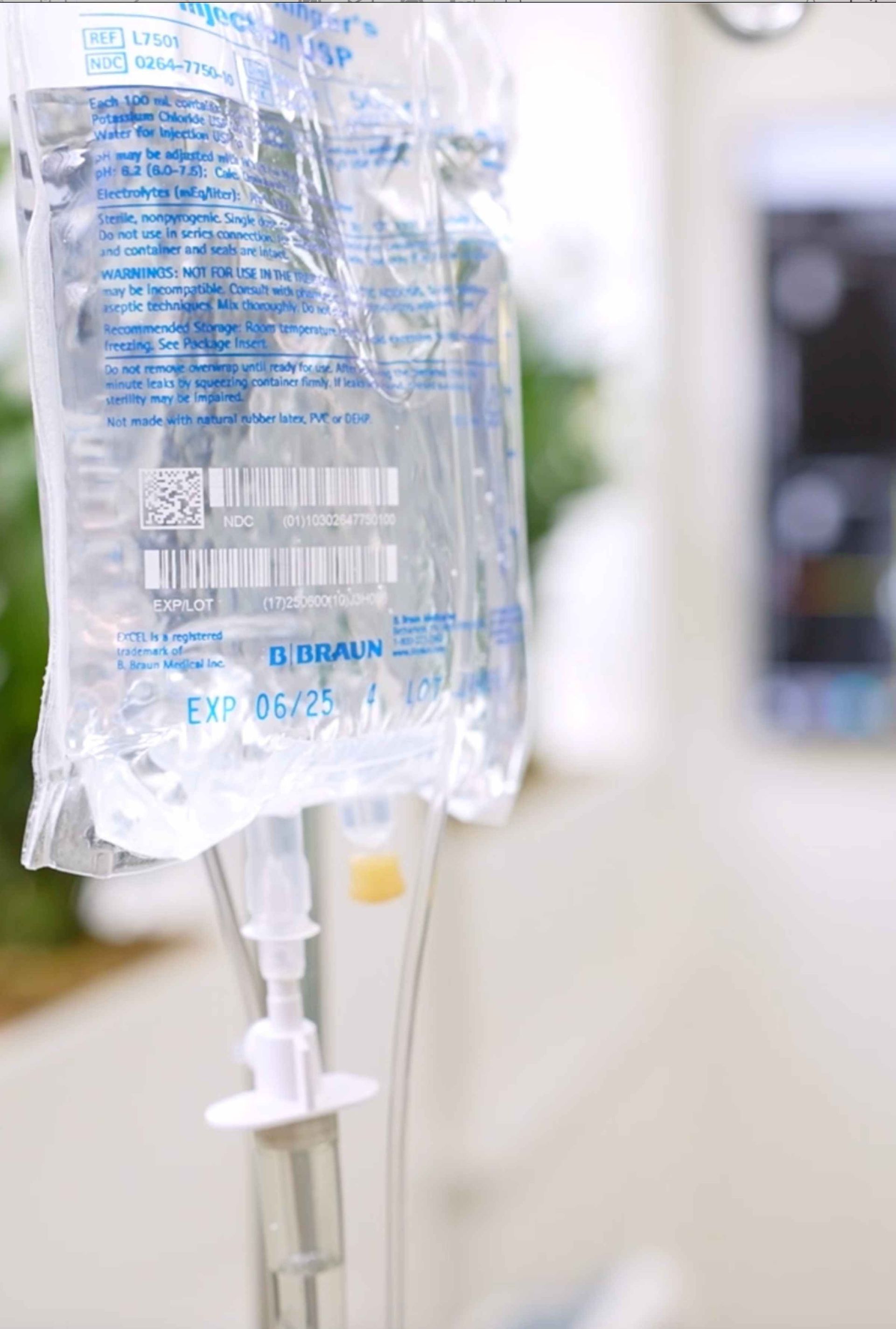 Intravenous (IV) bag filled with clear liquid, hanging from a hook. The bag has an expiration date of 05/25.