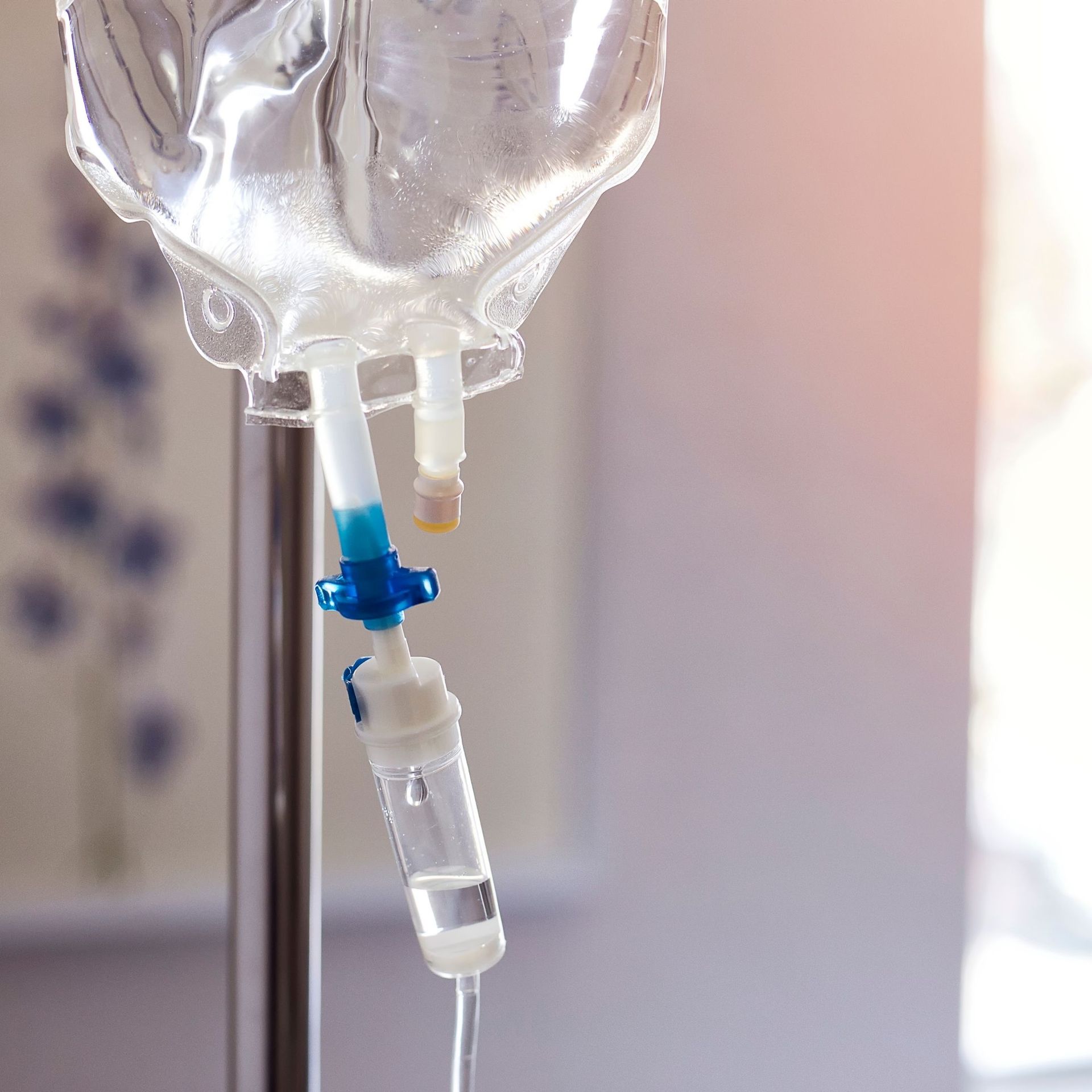 Intravenous (IV) bag hanging on a metal pole, dripping fluids. Blue and white control valve with tubing.