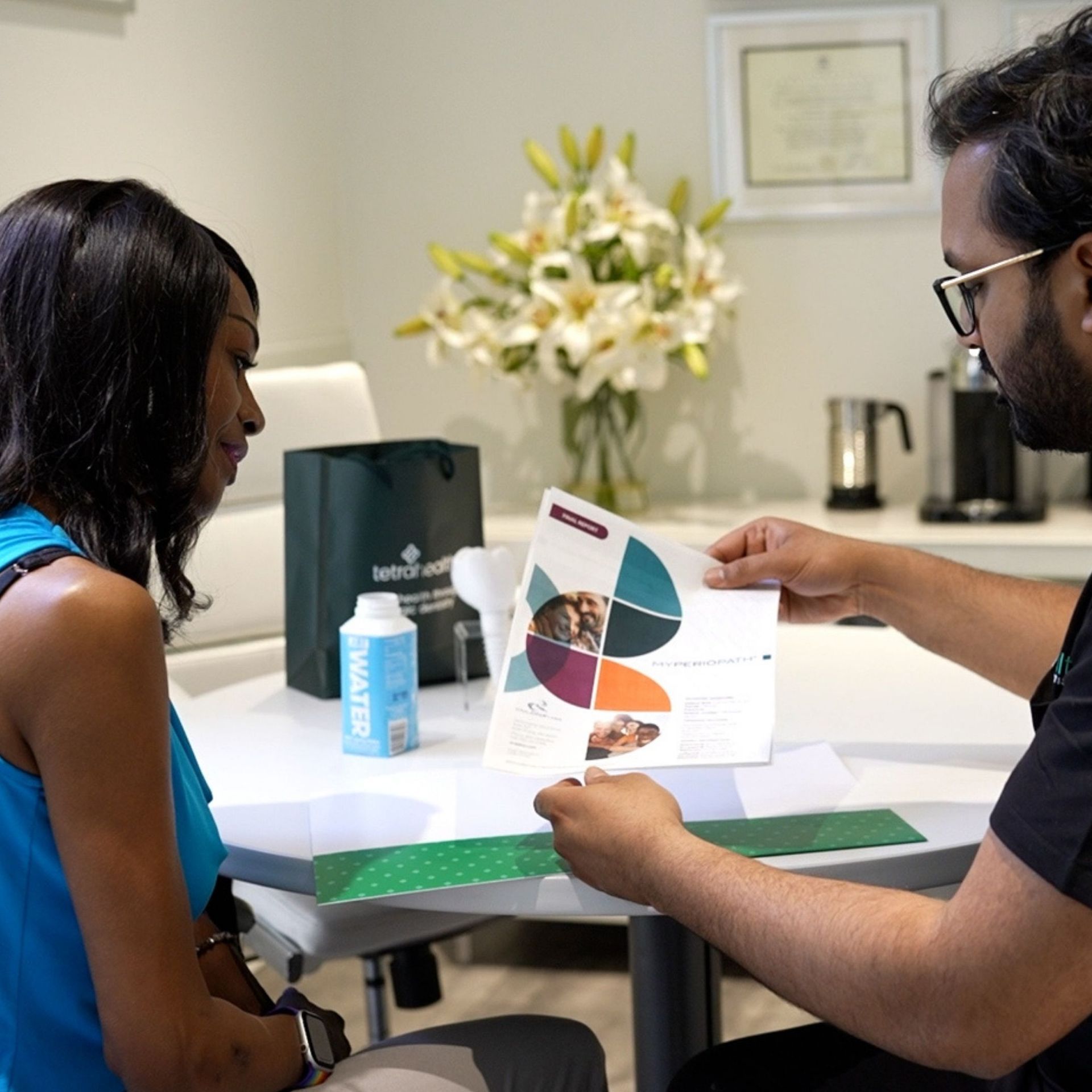 A healthcare professional reviews a food chart with a seated Black woman at a table. The woman appears engaged while the man points to the chart.