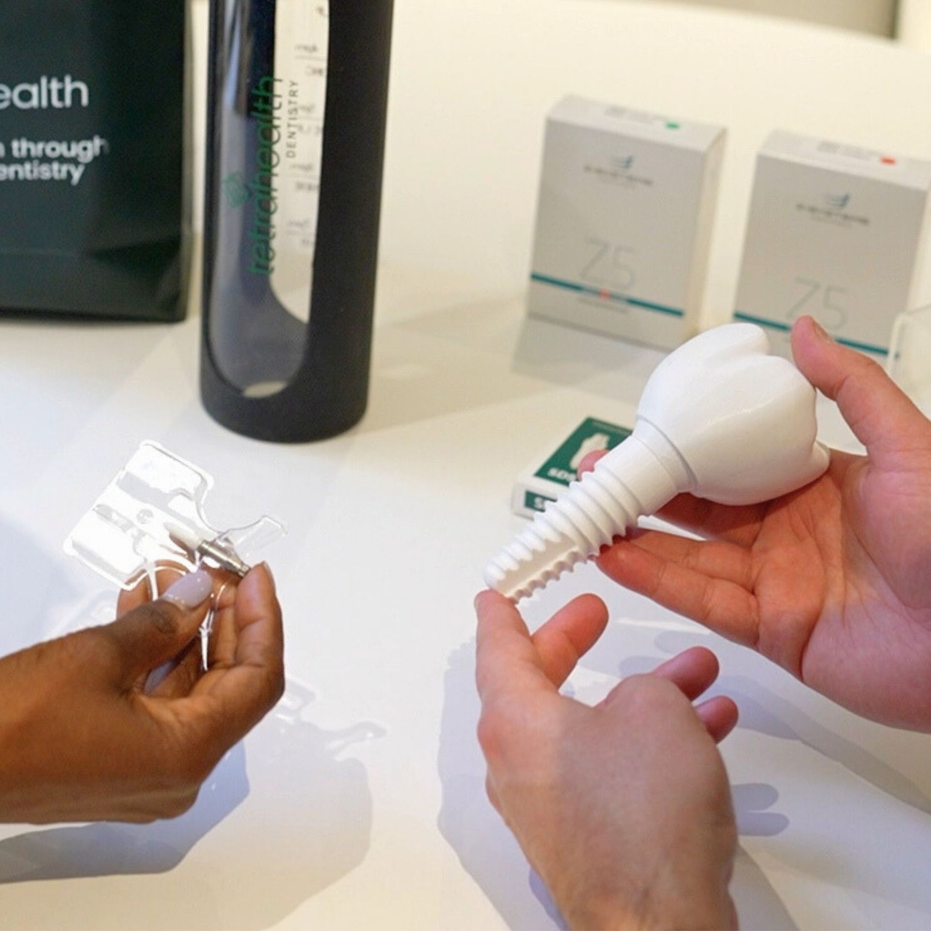Two people hold a dental model and clear aligner, with product packaging and water bottle on a white table.