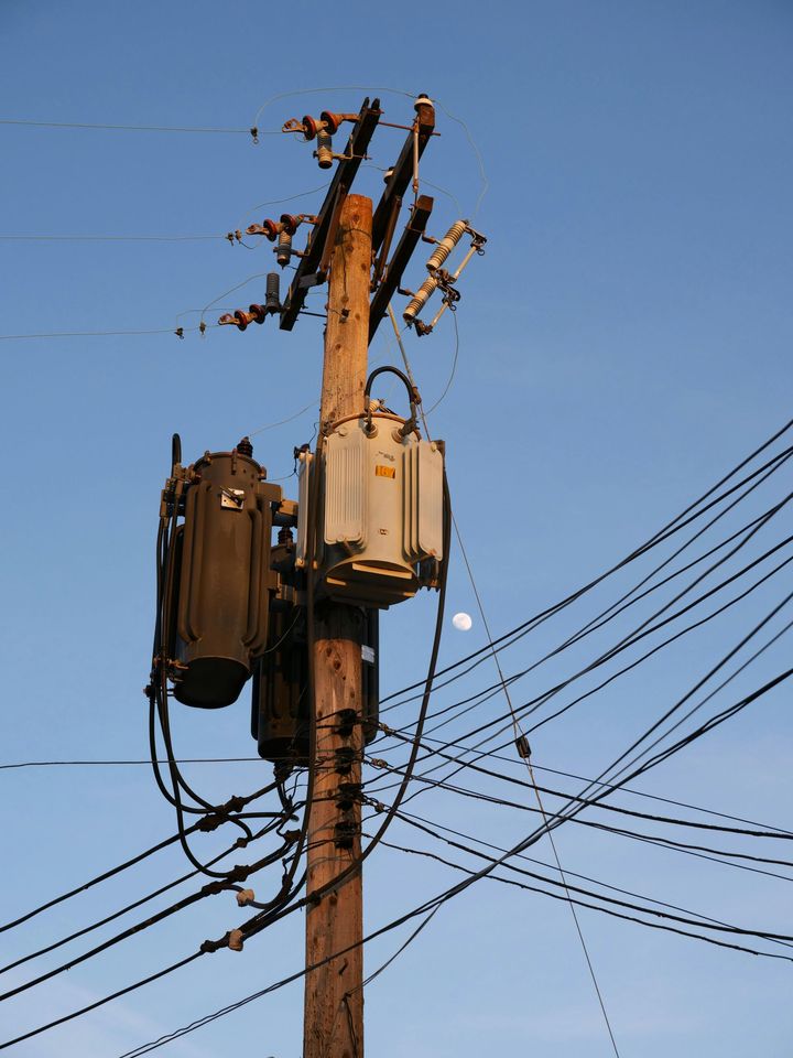 Utility pole with transformer and tangled overhead power lines against a blue sky