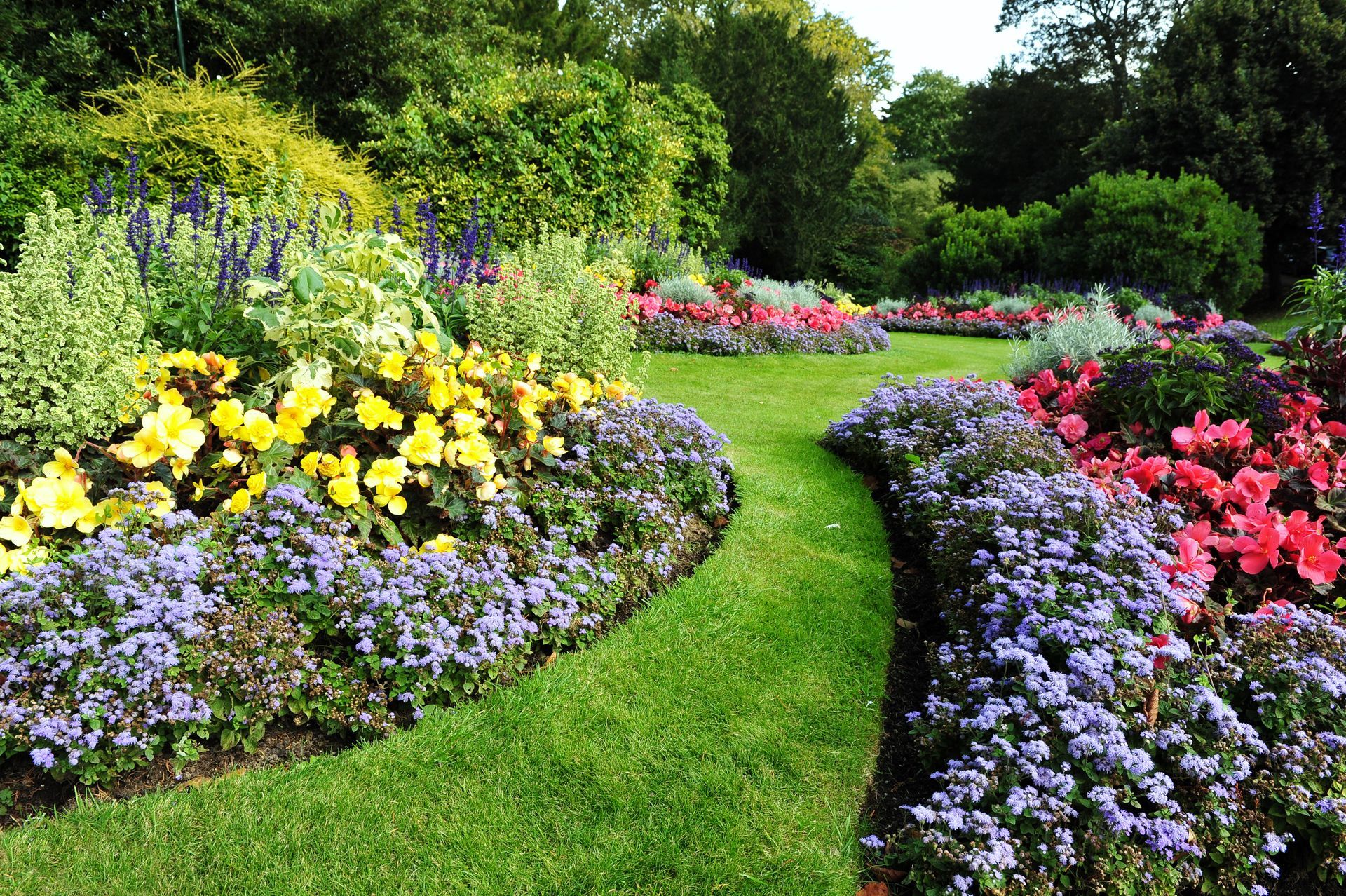 A curving grassy path winds through colorful flower beds in a garden.