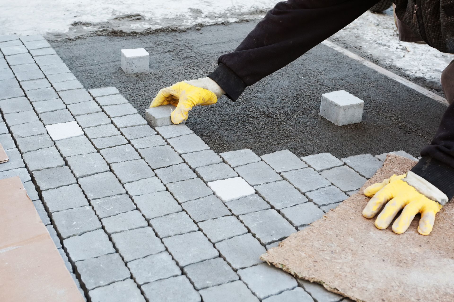 Person in yellow gloves laying gray paving stones outdoors.