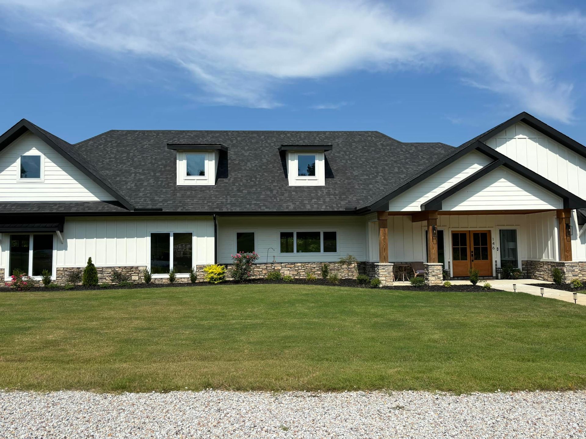 Single-story white house with dark roof and large front lawn under a blue sky