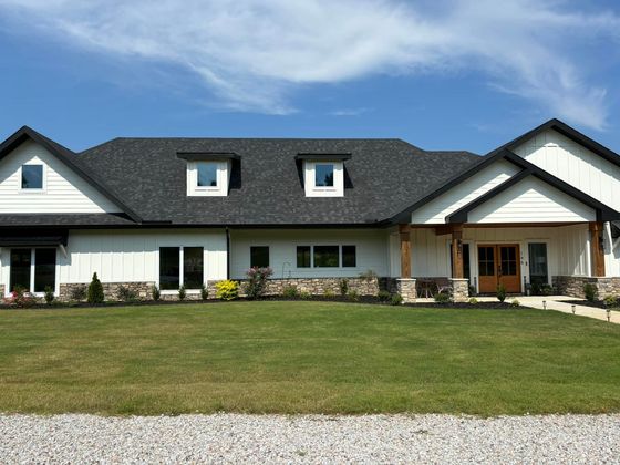 Large white suburban house with dark roof, front porch, and wide green lawn under a blue sky