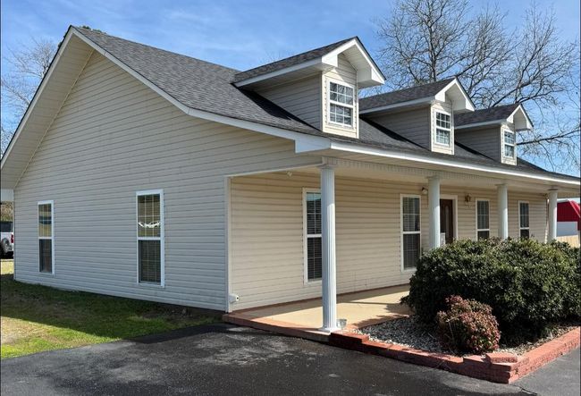 Yellow-sided house with white porch and trim, seen from the side under bright sunlight