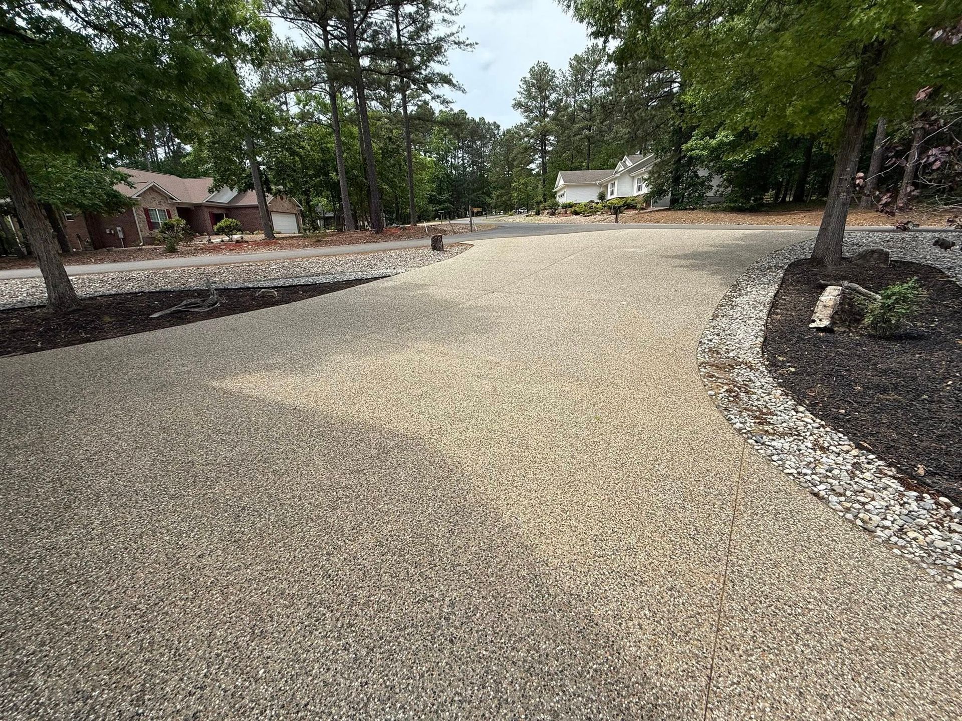 Gravel driveway curving through a wooded residential area with houses and landscaped beds