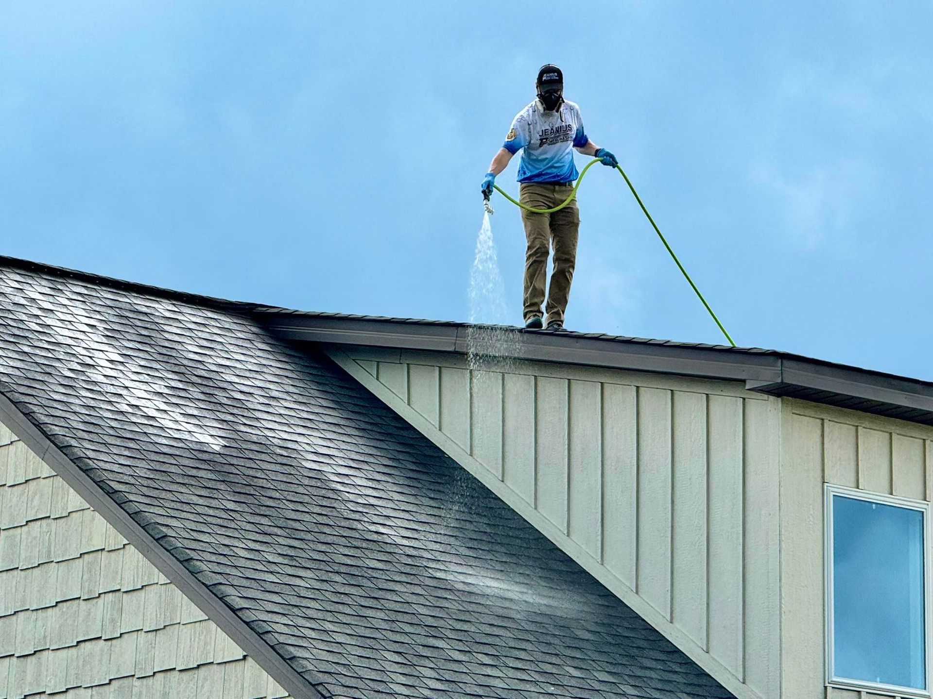 Worker on a shingled roof using a harness and tool, inspecting or repairing the roof.