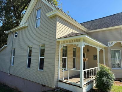 Yellow house exterior with white porch and tan roof, viewed from the side