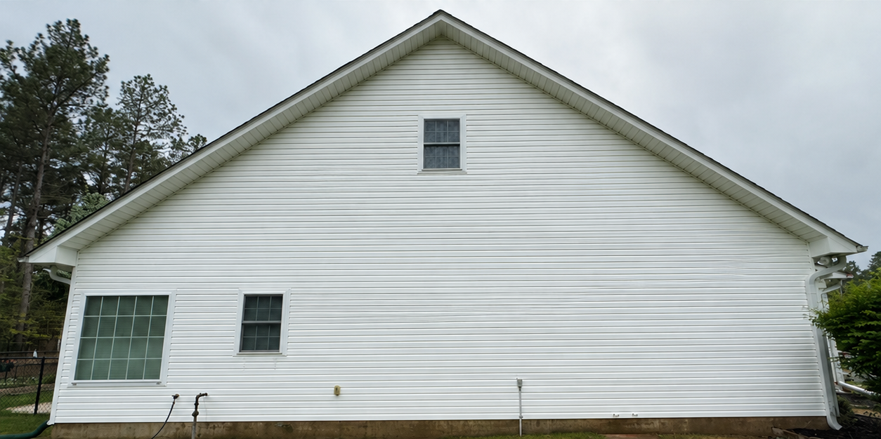 White house with horizontal siding, gabled roof, and several windows on the side view