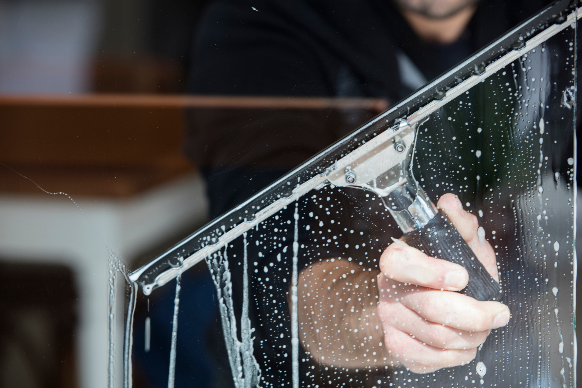 Hand cleaning a glass window with soap suds and water droplets