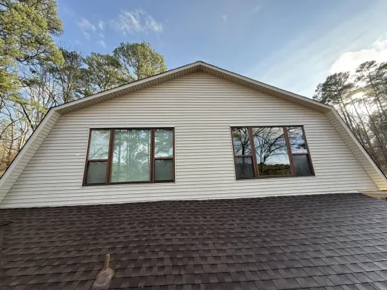 House exterior with beige siding, dark roof, and two windows under a blue sky