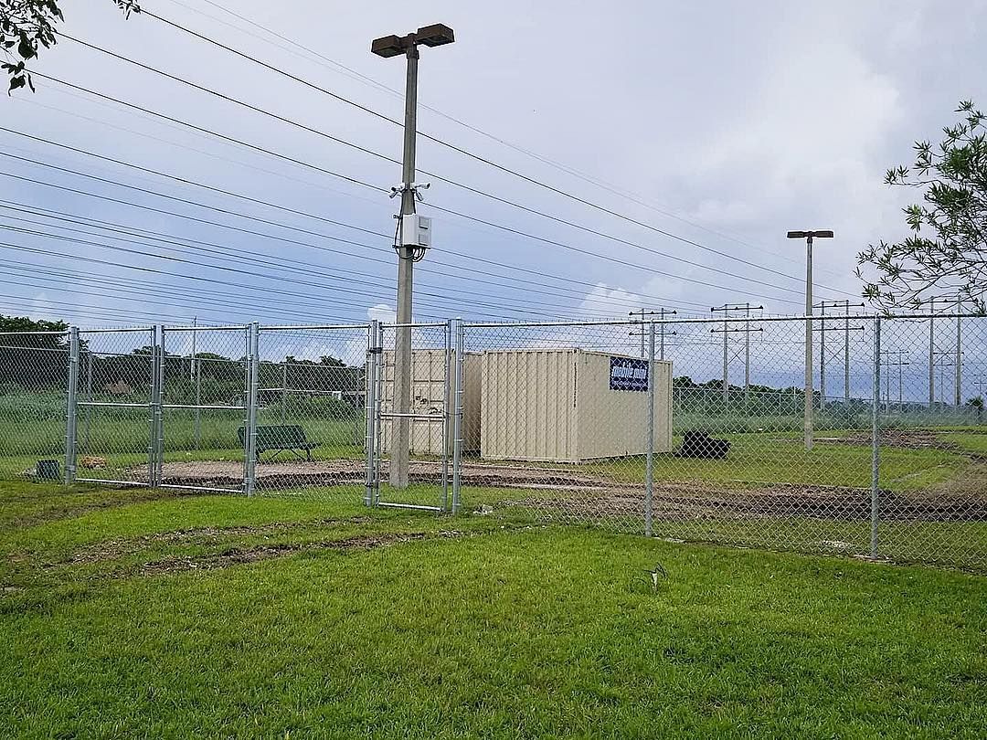 A chain link fence surrounds a grassy field with a building in the background.