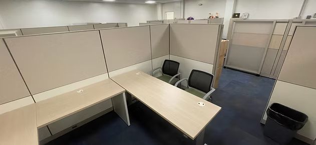 A cubicle in an office with a desk and chairs.