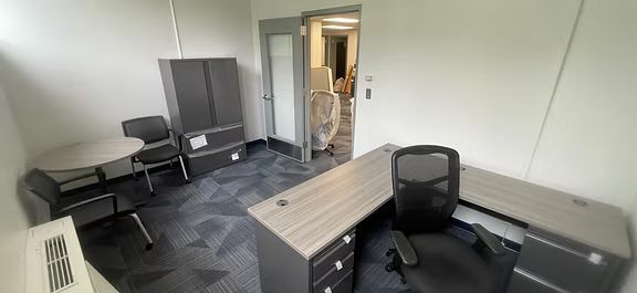 A small office with a desk , chair , table and cabinets.