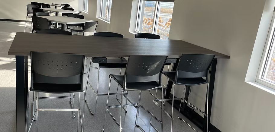 A long table with chairs in a room with a lot of windows.