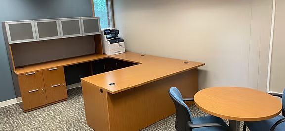 A small office with a desk , chairs , and a round table.