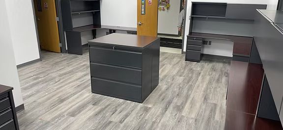 A room with a wooden floor , a dresser , a desk , and a door.