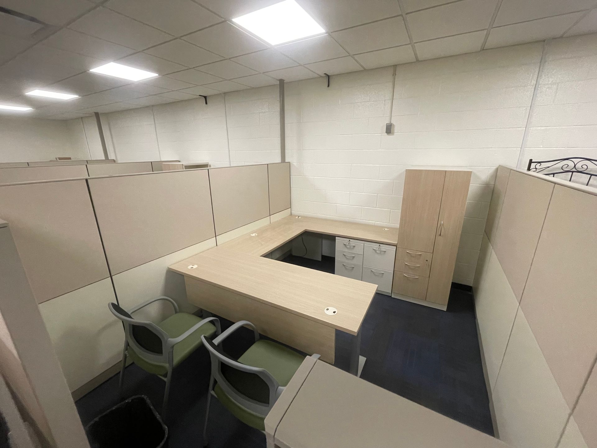 A cubicle in an office with a desk and chairs.
