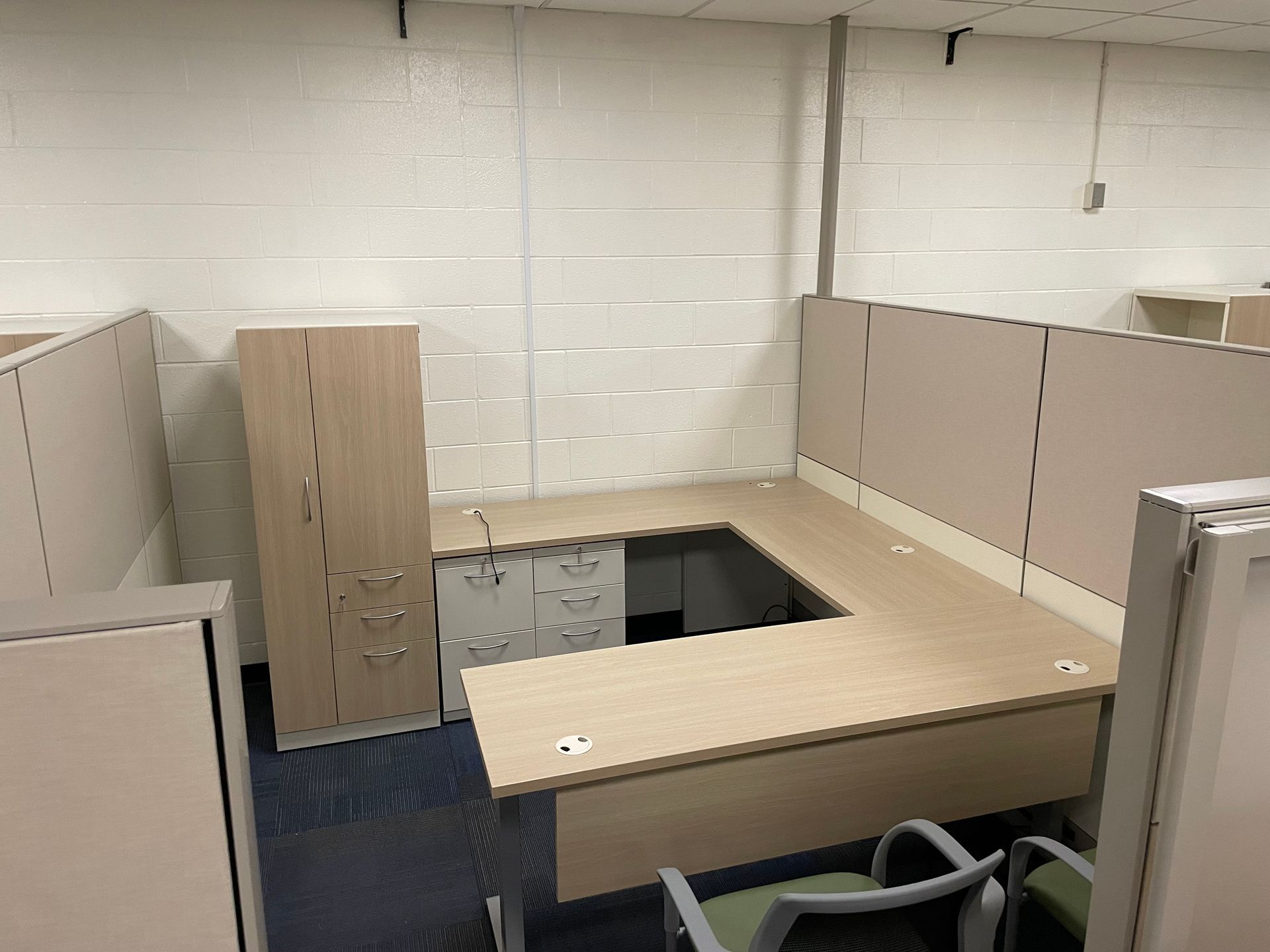A cubicle in an office with a desk and chairs.