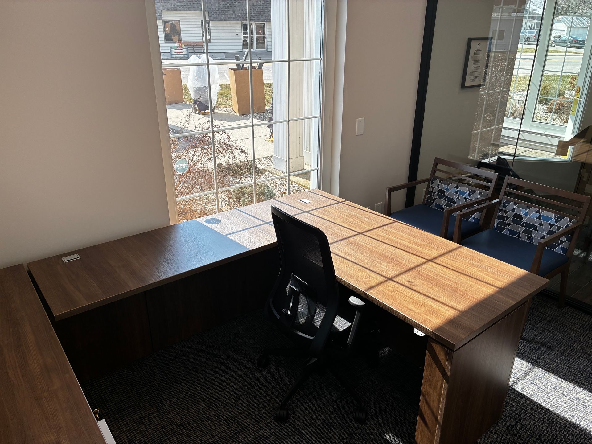 A small office with a desk and chairs in front of a window.