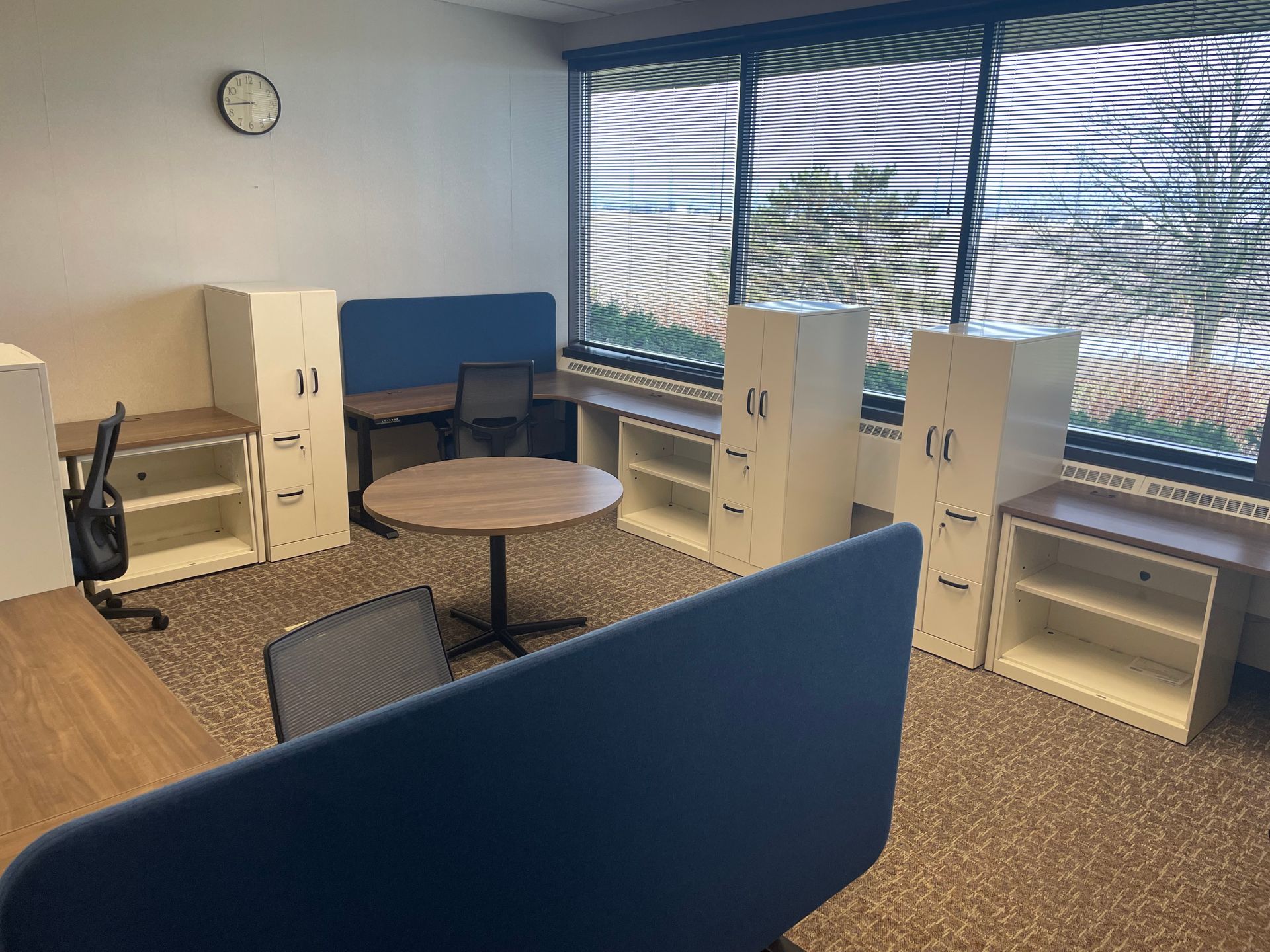 A room with a table , chairs , filing cabinets and a clock on the wall.