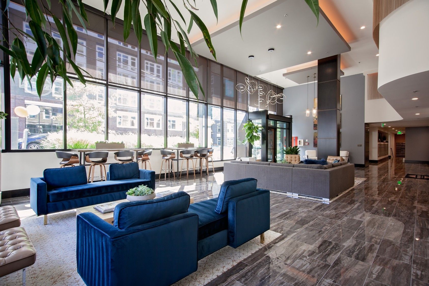 Modern hotel lobby with blue chairs, large windows, and a central fireplace lounge area