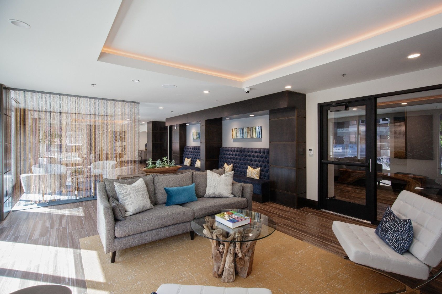 Modern living room with gray sofas, teal pillows, dark wood accents, and recessed ceiling lights