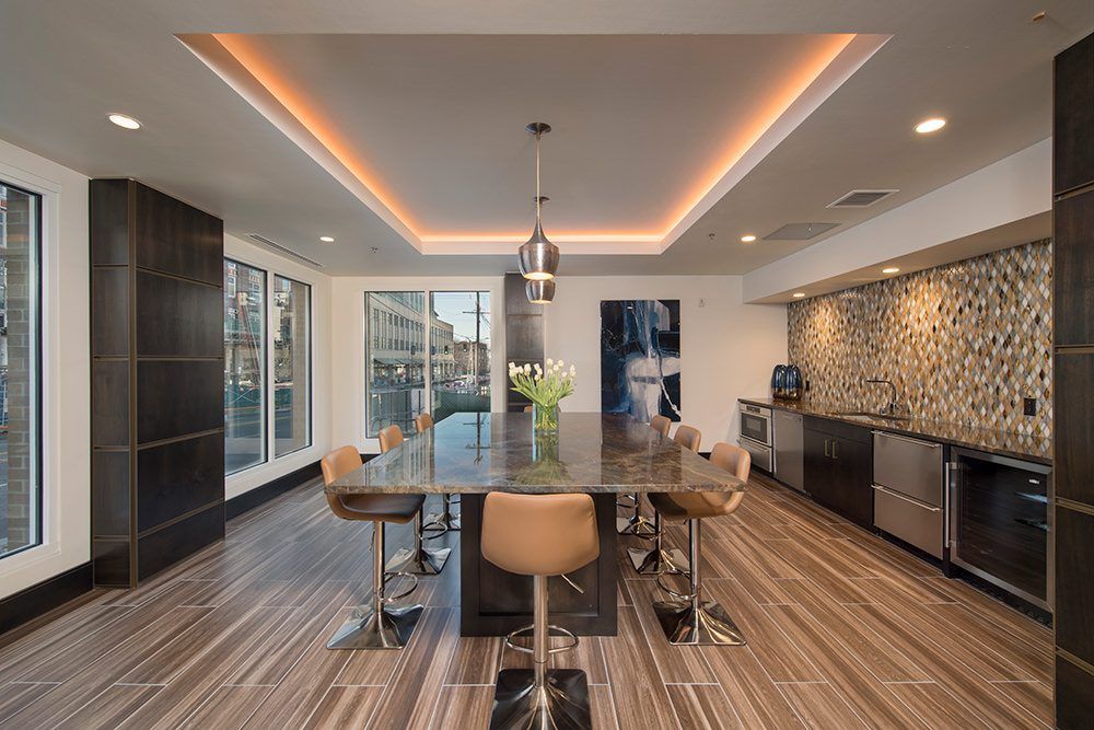 Modern dining room with a long table, tan chairs, striped wood floor, and warm ceiling lights